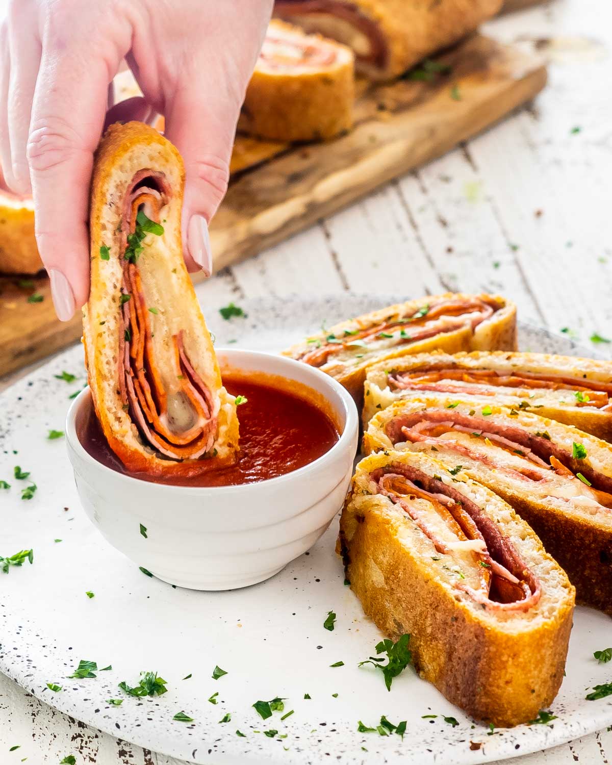 a hand dipping a piece of stromboli in a bowl with marinara sauce.