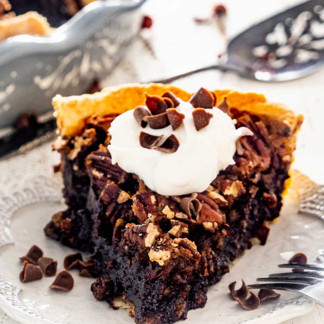 a slice of chocolate pecan pie topped with a dollop of whipped cream.