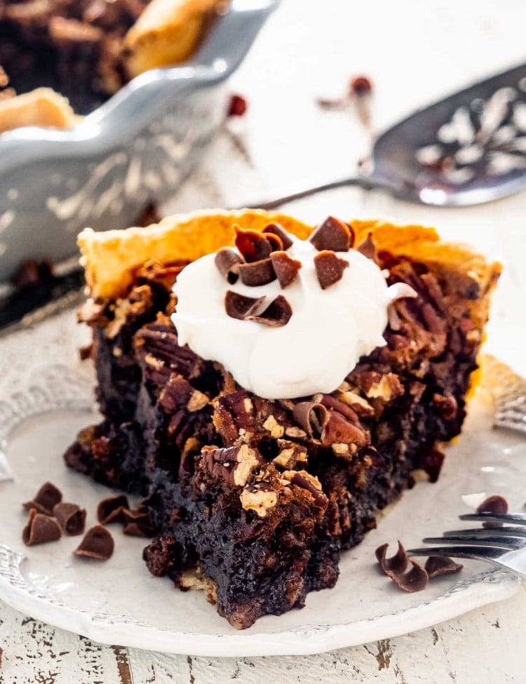 a slice of chocolate pecan pie topped with a dollop of whipped cream.