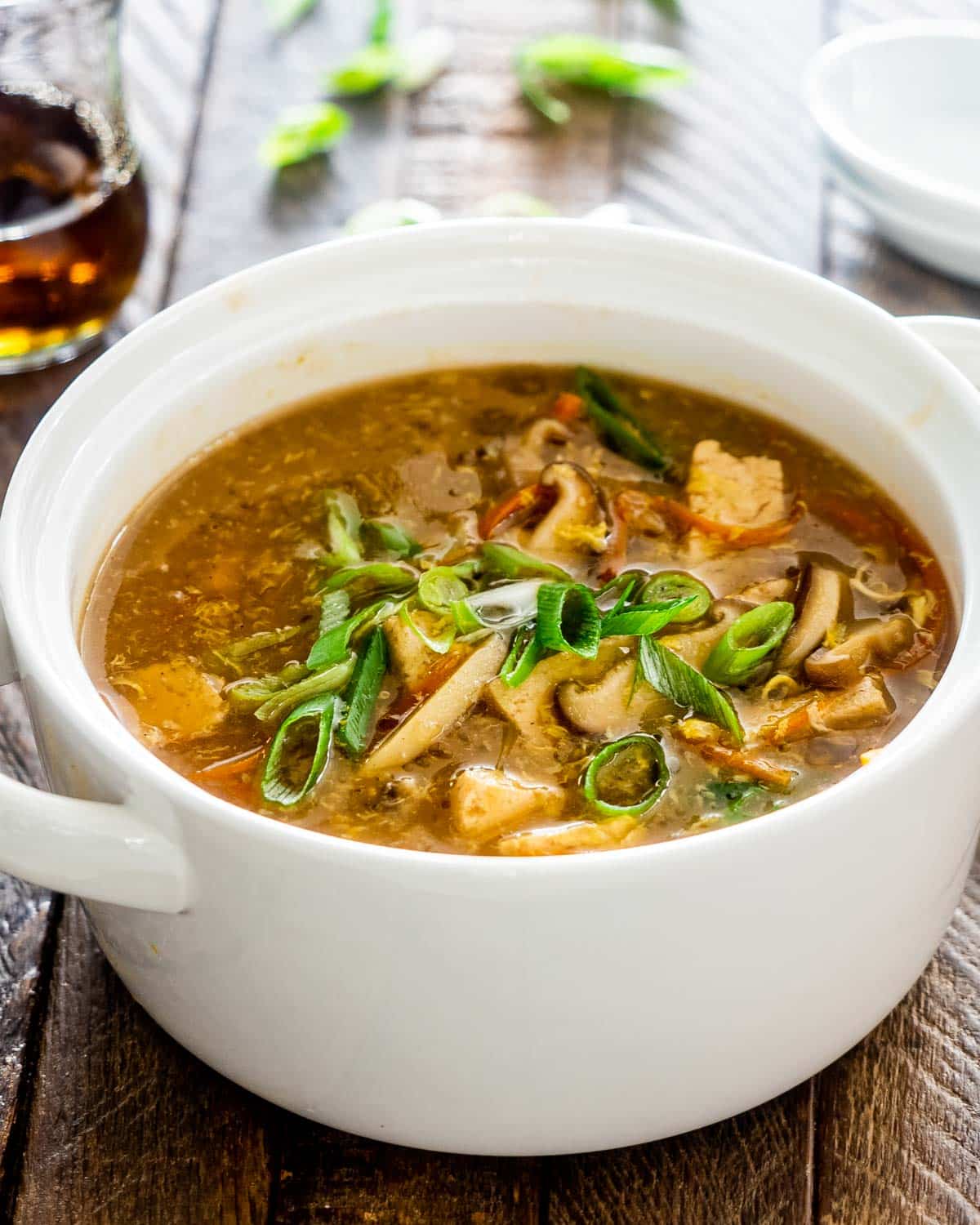 hot and sour soup in a white bowl garnished with green onions.