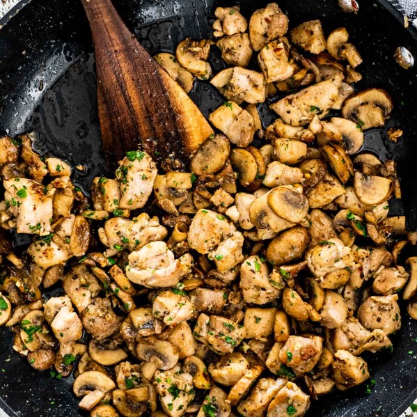 mushroom chicken bites in a black skillet with a wooden spatula in it.