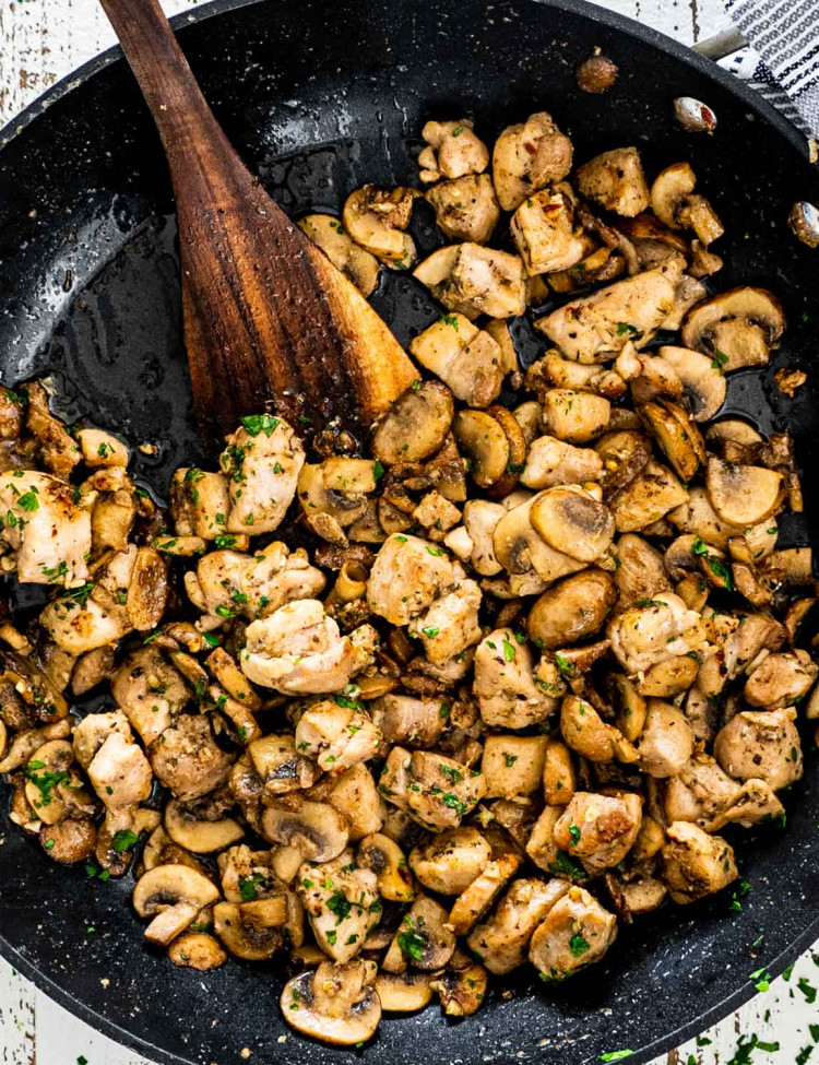 mushroom chicken bites in a black skillet with a wooden spatula in it.