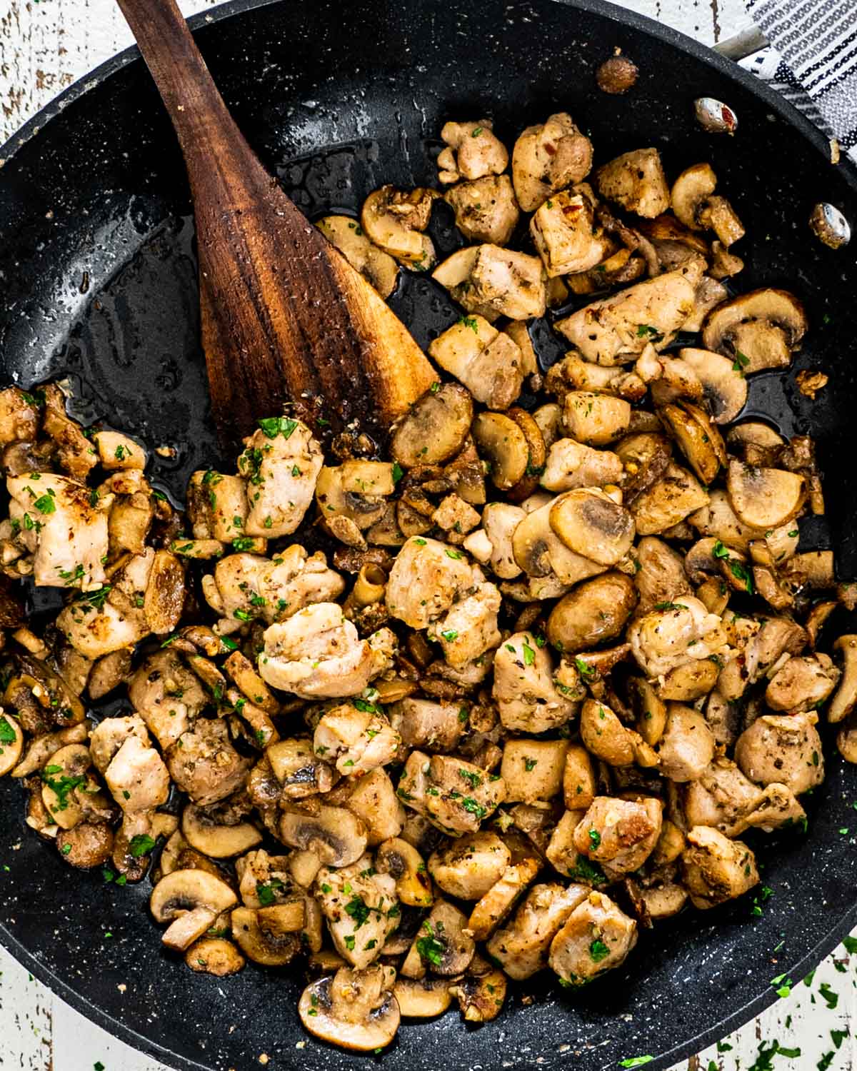 mushroom chicken bites in a black skillet with a wooden spatula in it.