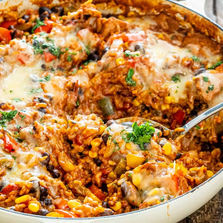 a serving spoon in a pot filled with tex mex chicken and rice.