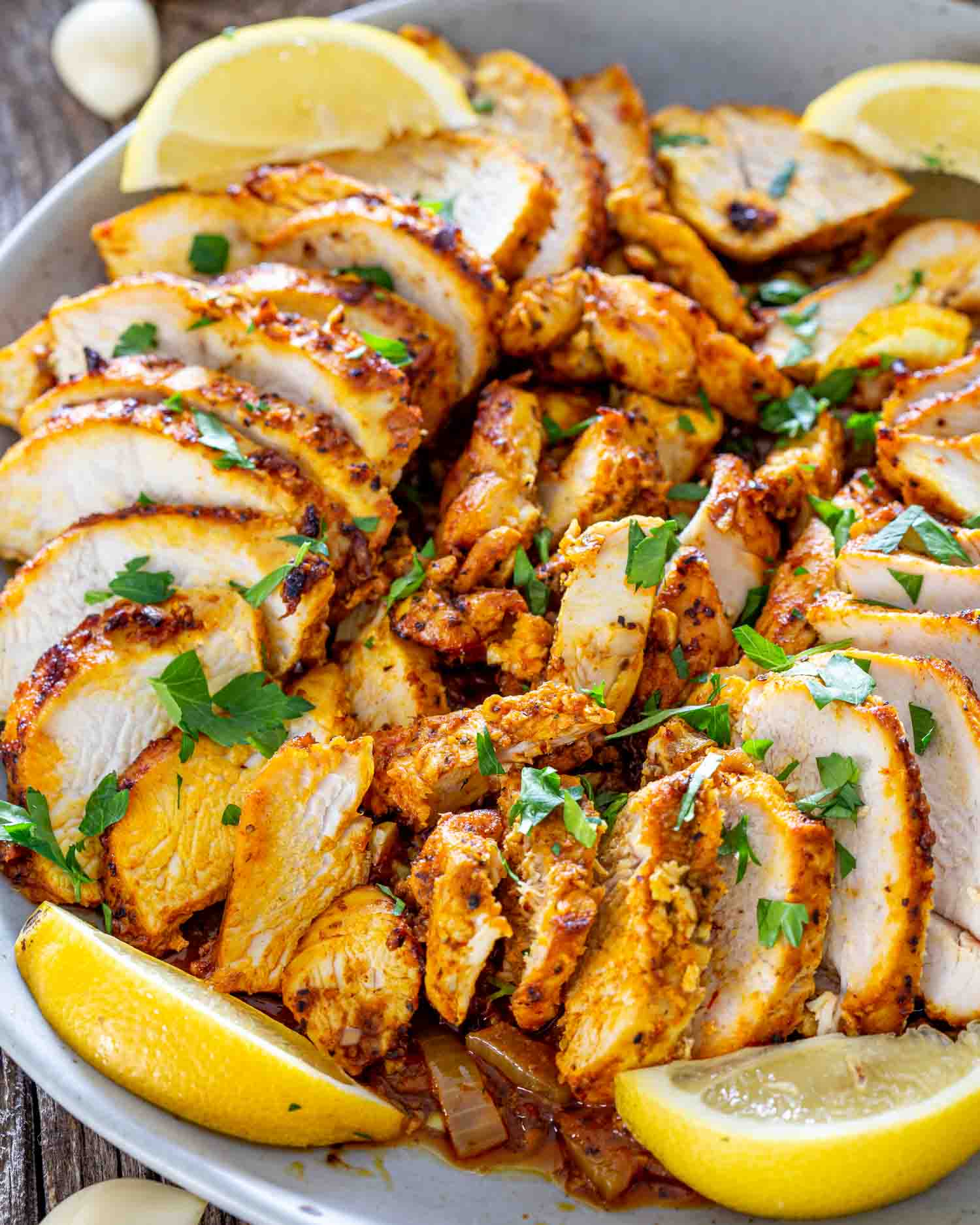 sliced chicken shawarma in a white bowl garnished with parsley and lemon wedges.