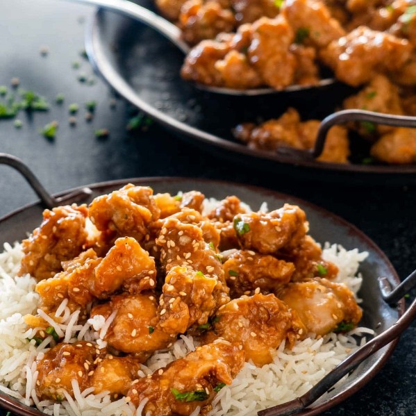 chinese honey chicken on a bed of rice garnished with sesame seeds.