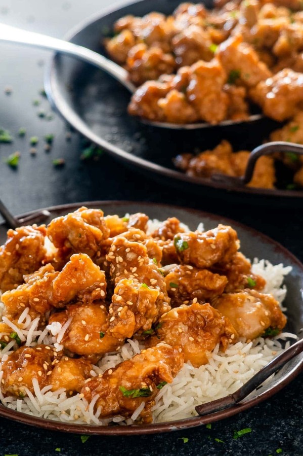 chinese honey chicken on a bed of rice garnished with sesame seeds.