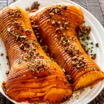 two halves of a honey roasted butternut squash on a platter roasted with sugar pecans.
