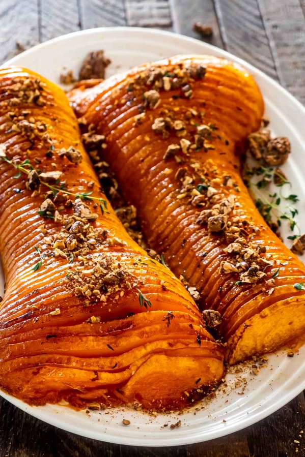 two halves of a honey roasted butternut squash on a platter roasted with sugar pecans.