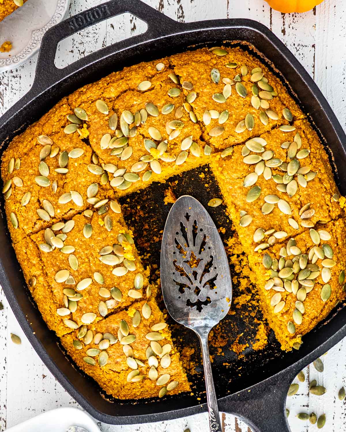 a skillet with pumpkin maple cornbread topped with pepitas and cut into slices.