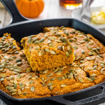 a skillet with pumpkin maple cornbread topped with pepitas and cut into slices.