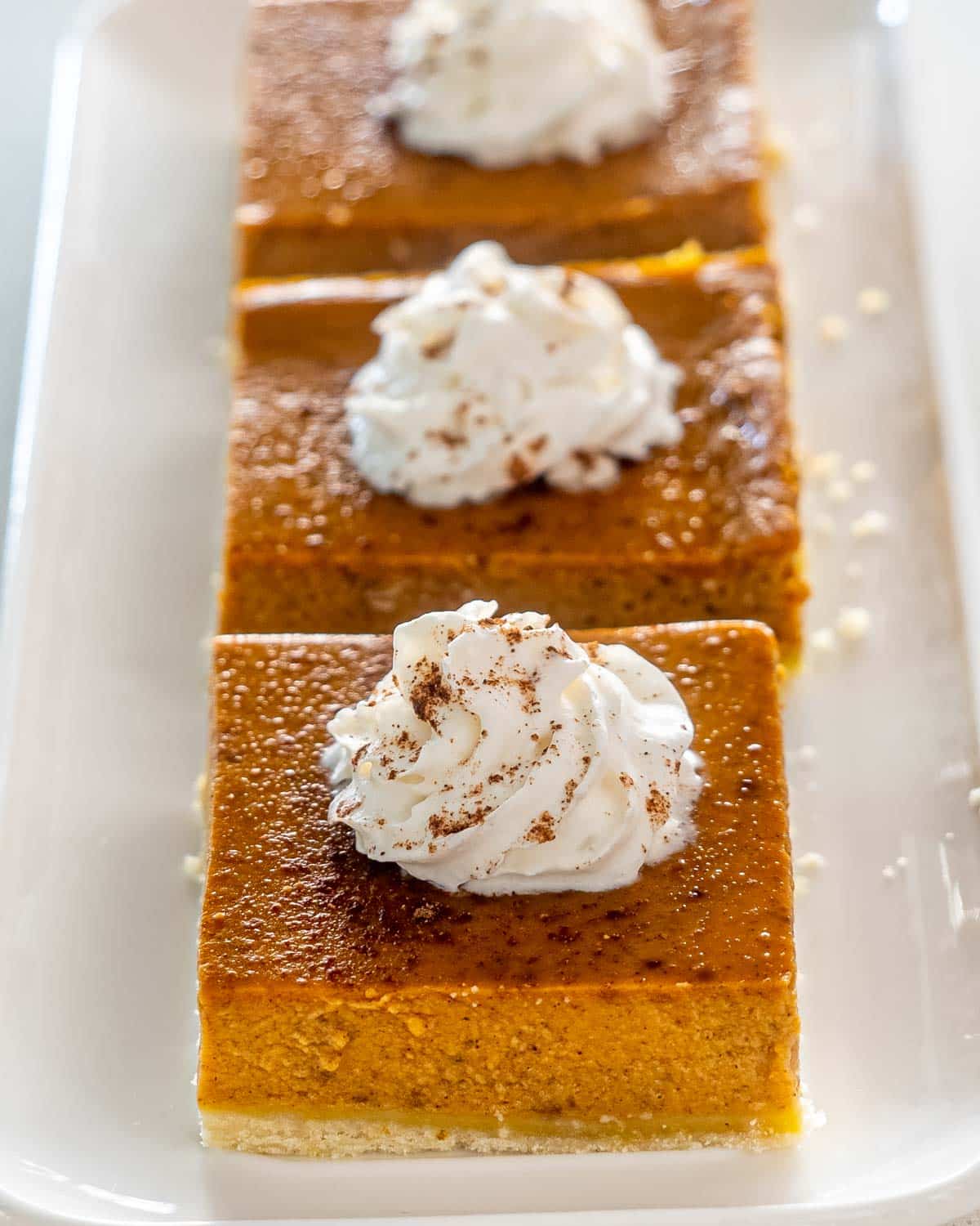 3 pumpkin pie bars on a white plate topped with whipped cream.