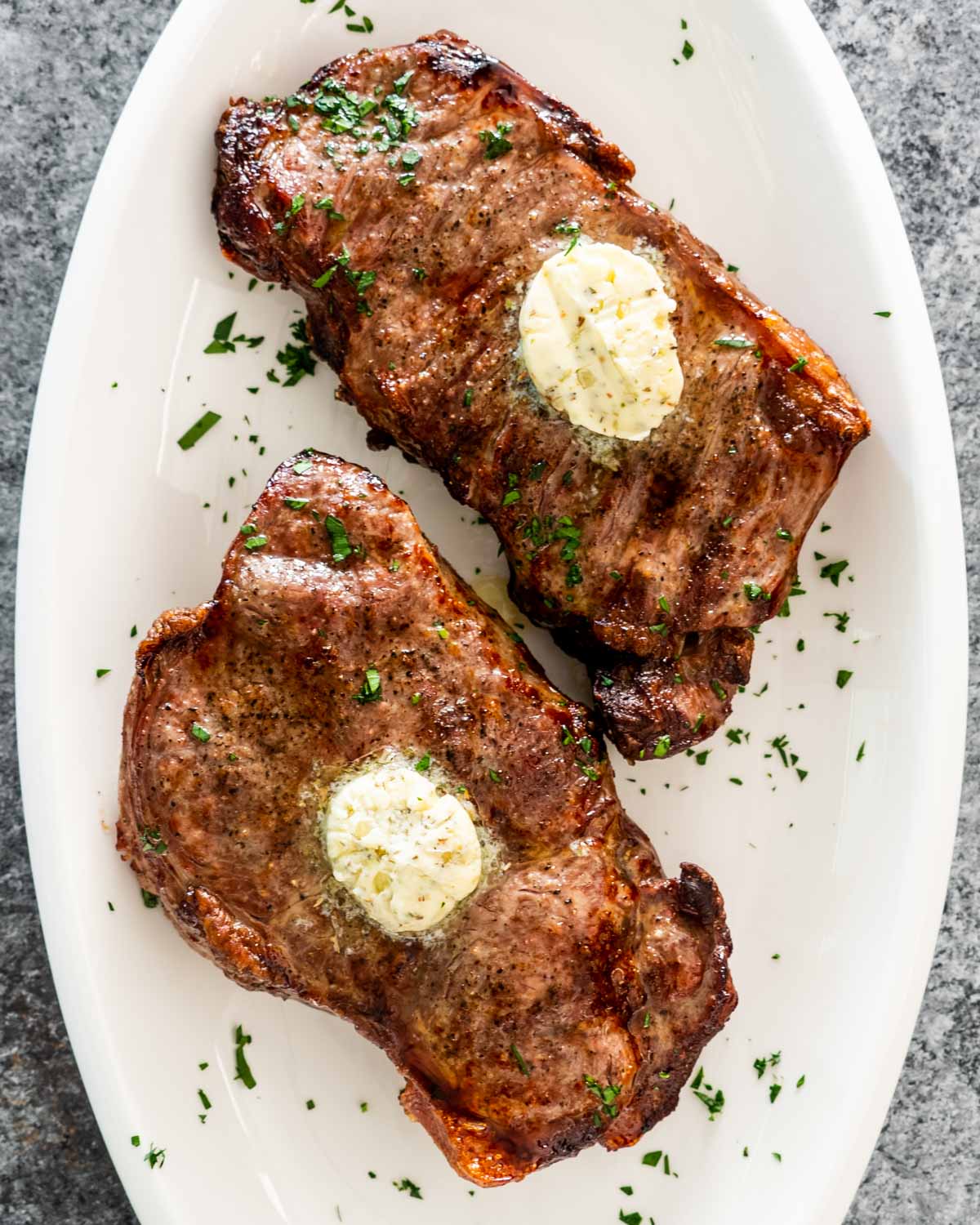 2 steaks with compound butter made in an air fryer on a white platter.