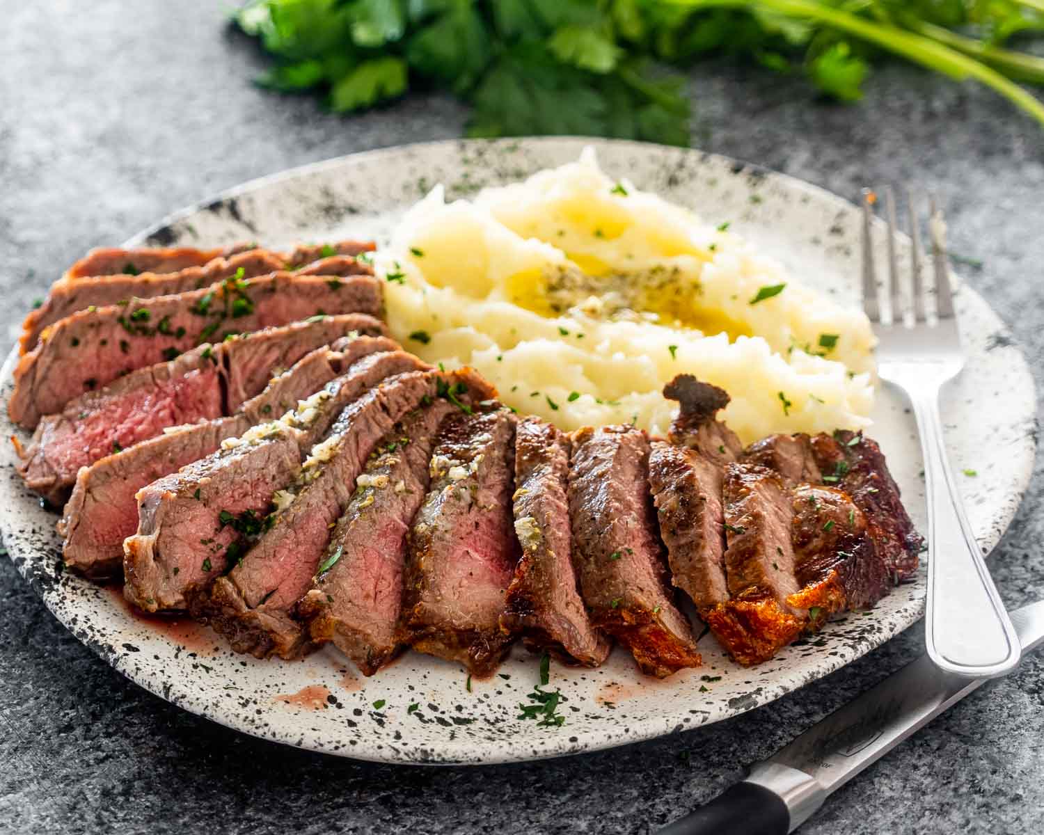 sliced up steak with mashed potatoes on a plate.