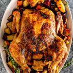 a roasted chicken on a serving platter along some roasted root veggies.