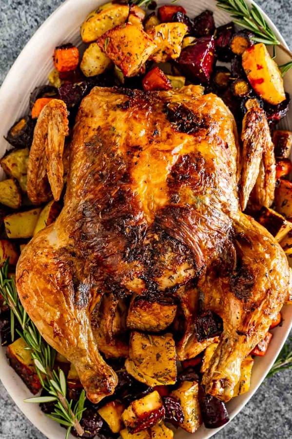 a roasted chicken on a serving platter along some roasted root veggies.
