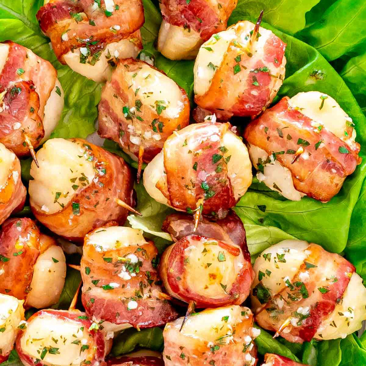 bacon wrapped scallops brushed with garlic butter on a bed of lettuce.