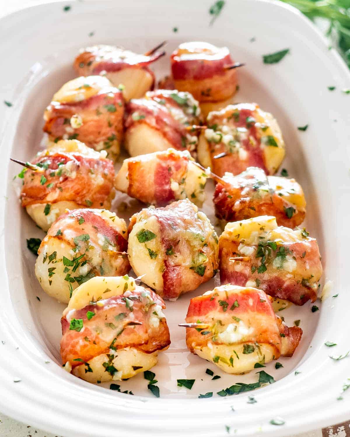 bacon wrapped scallops brushed with garlic butter on a white serving platter.
