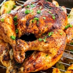 a whole roasted chicken on a roaster with potatoes.