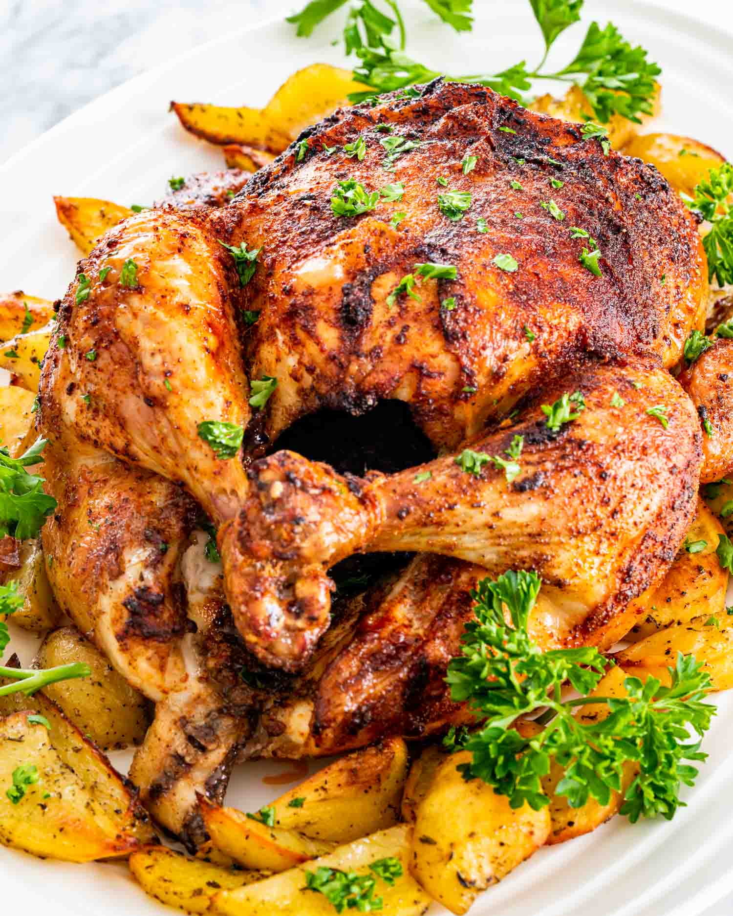 a complete roast chicken in a dish with roasted potatoes.