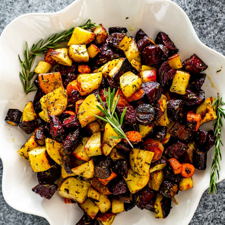 roasted root vegetables in a white bowl garnished with fresh rosemary.