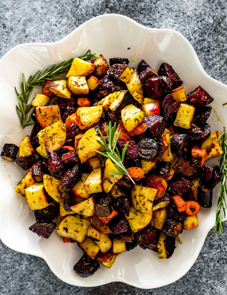 roasted root vegetables in a white bowl garnished with fresh rosemary.