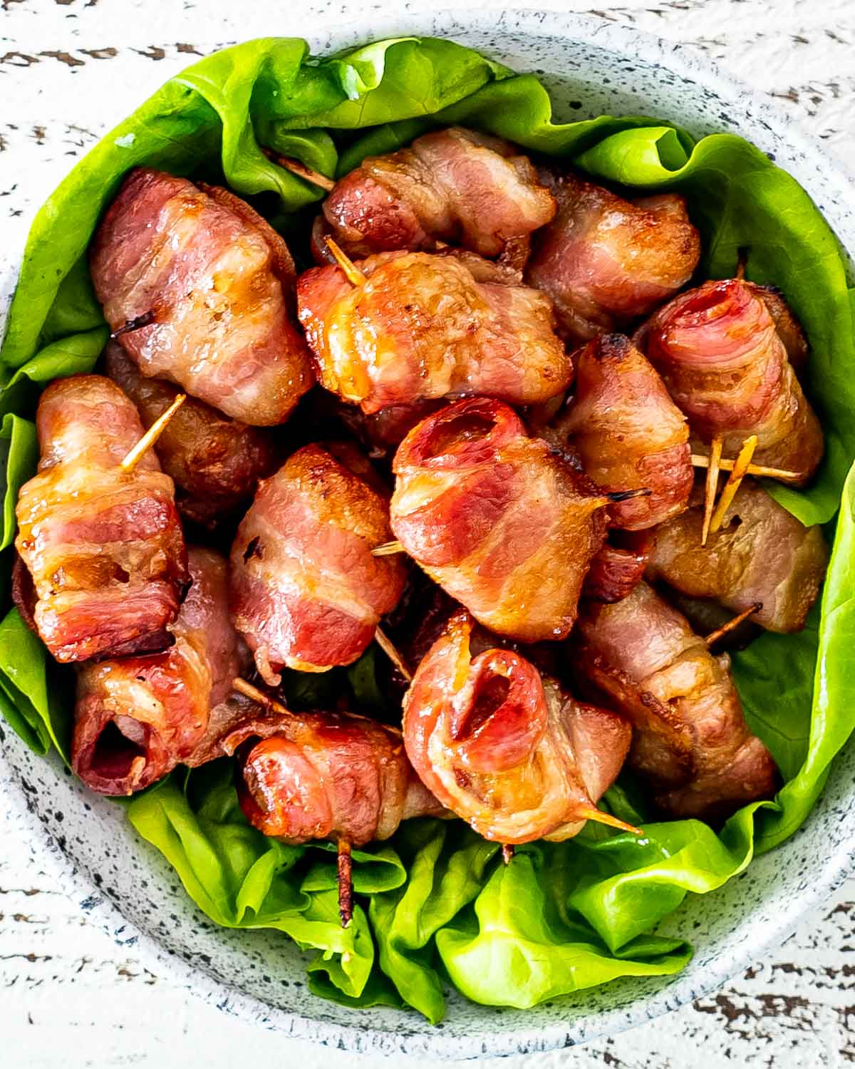 bacon wrapped water chestnuts on a bed of lettuce in a bowl.
