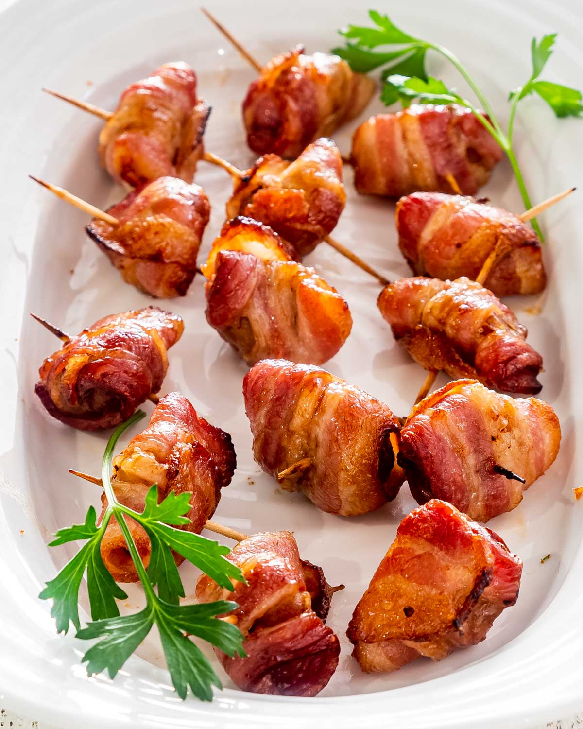 bacon wrapped water chestnuts on a serving platter garnished with parsley.