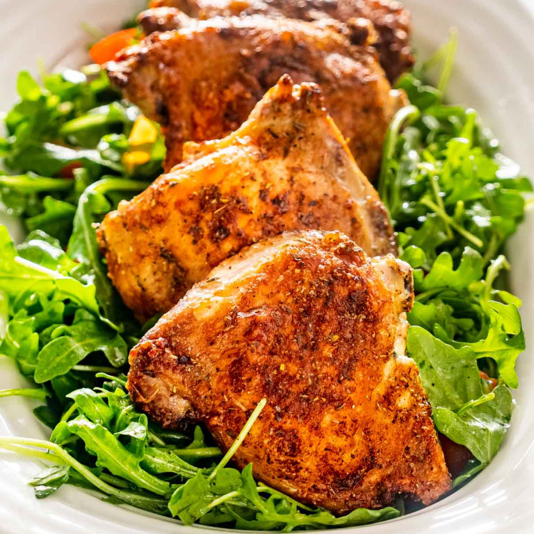 air fried chicken thighs on a serving platter over a greens salad.