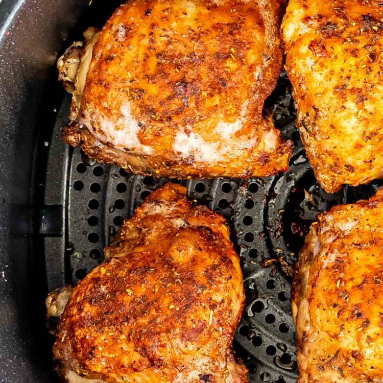 cooked chicken thighs in the basket of an air fryer.