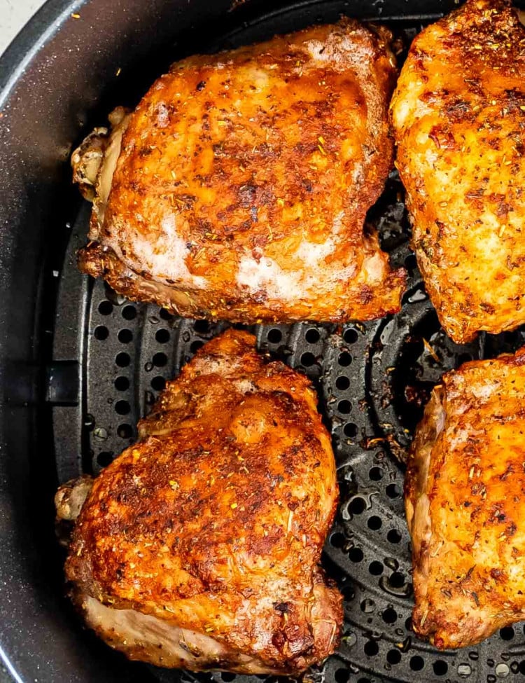 cooked chicken thighs in the basket of an air fryer.