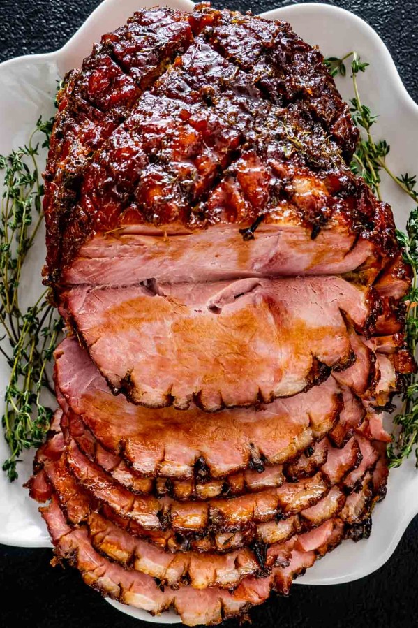 bourbon glazed ham on a white platter sliced garnished with fresh thyme.