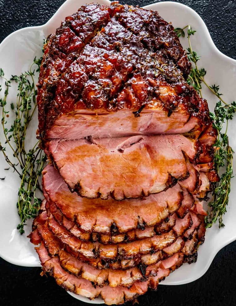 bourbon glazed ham on a white platter sliced garnished with fresh thyme.