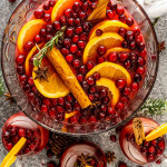 christmas punch in a punch bowl with a few cups filled with punch around it.