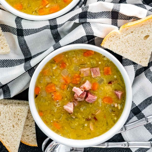 split pea soup in a white bowl with a couple slices of bread around it.