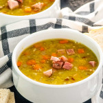 split pea soup in a white bowl with a couple slices of bread around it.