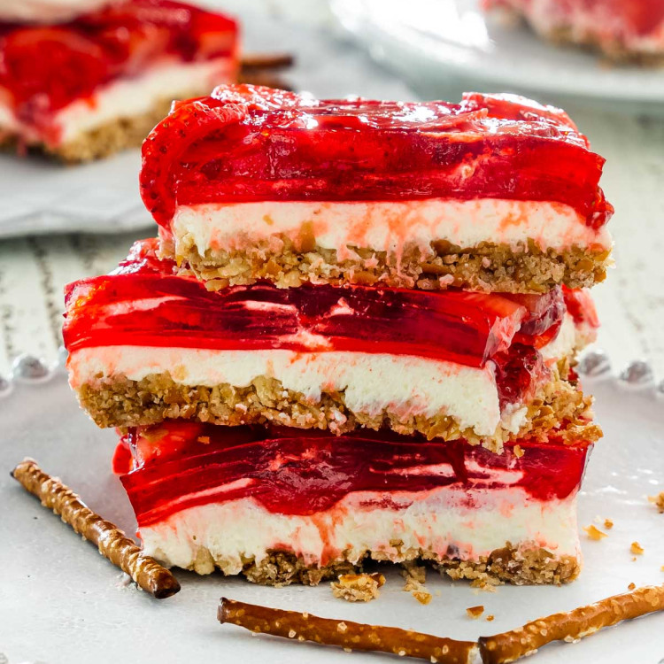 3 slices of strawberry pretzel salad stacked on top of each other on a white dessert plate.