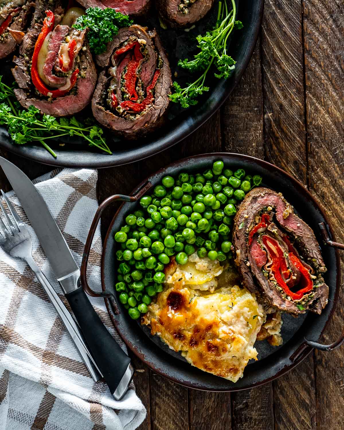 a serving of italian stuffed flank steak with a side of peas and scalloped potatoes.