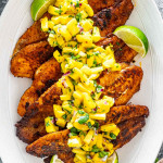 blackened fish on a white platter topped with mango salsa.