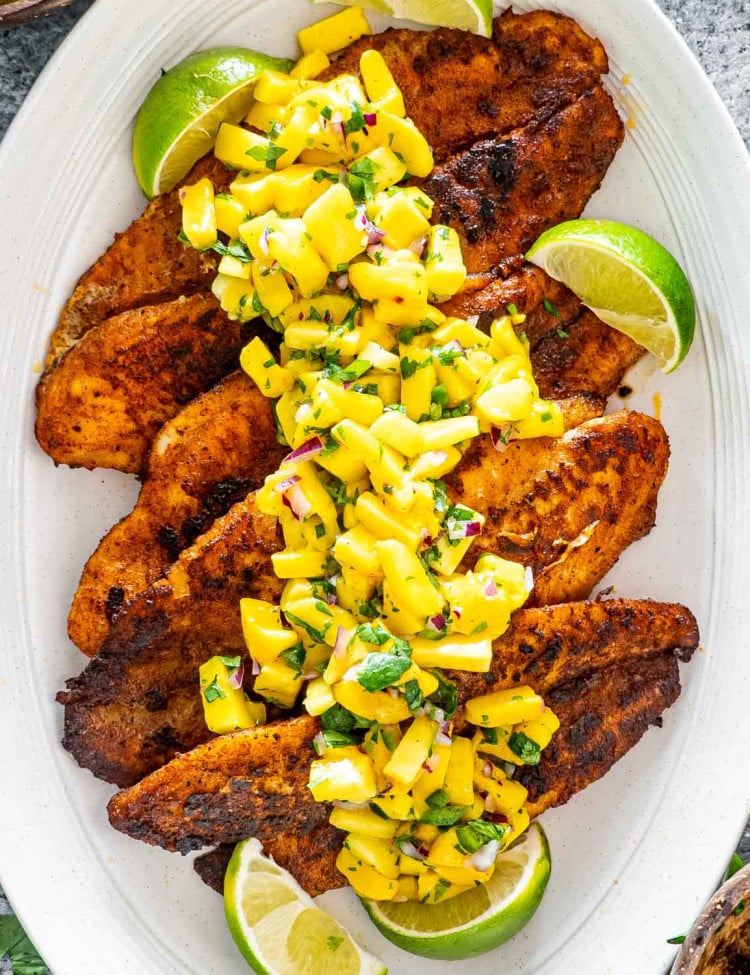 blackened fish on a white platter topped with mango salsa.