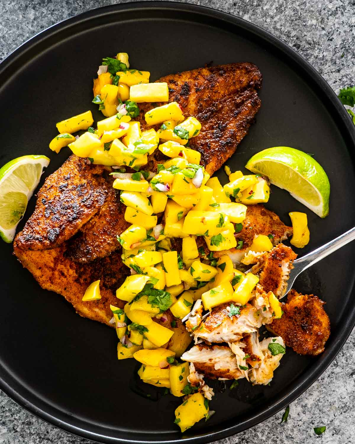 blackened fish on a black plate topped with mango salsa.