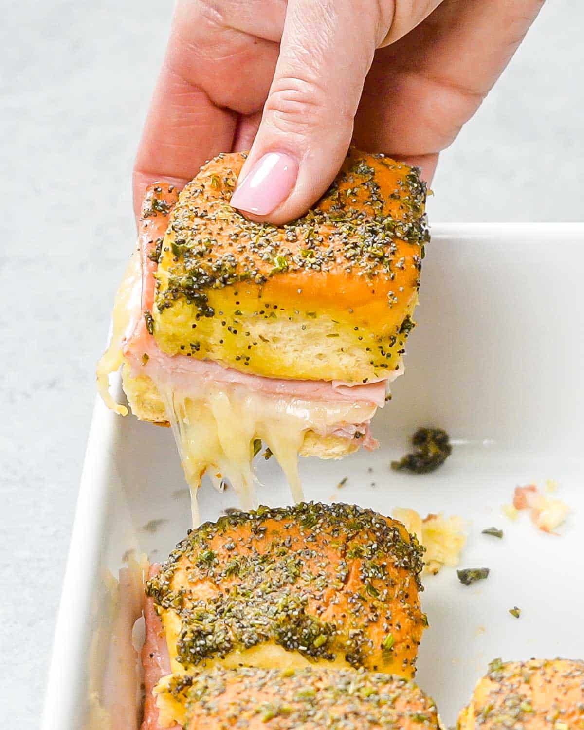 a hand holding a ham and cheese slider.