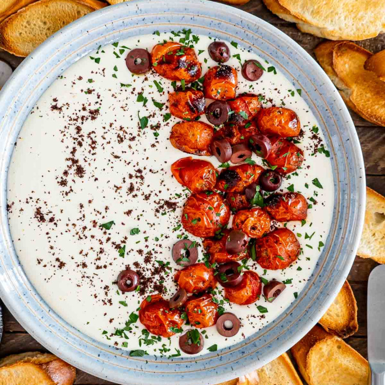 a bowl with whipped feta dip topped with roasted tomatoes surround by pita chips.
