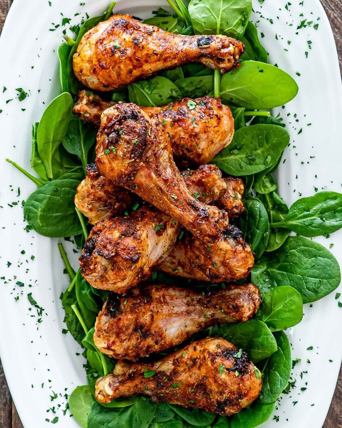 chicken drumsticks made in the air fryer on a bed of spinach on a white platter.