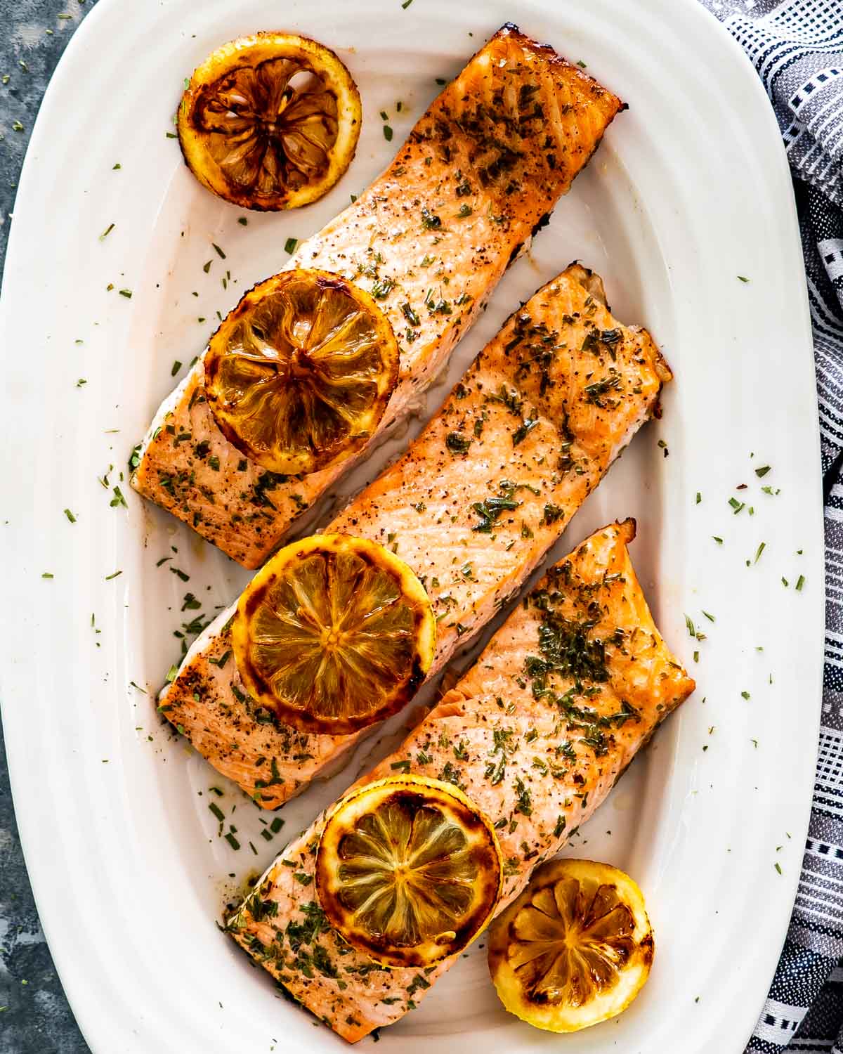 baked salmon with lemon slices on a white platter.