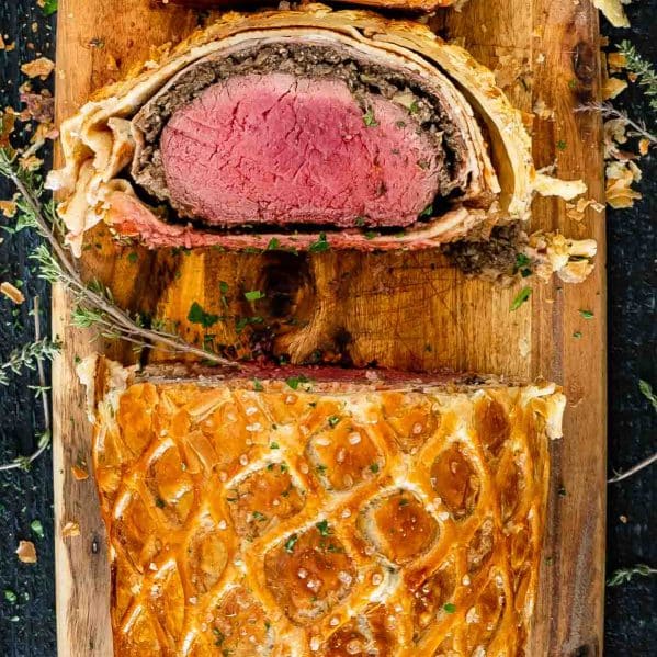 a beef wellington with 2 slices cut on a cutting board.