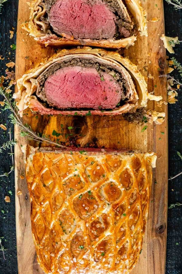a beef wellington with 2 slices cut on a cutting board.