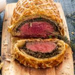 a beef wellington with 1 slices cut on a cutting board.