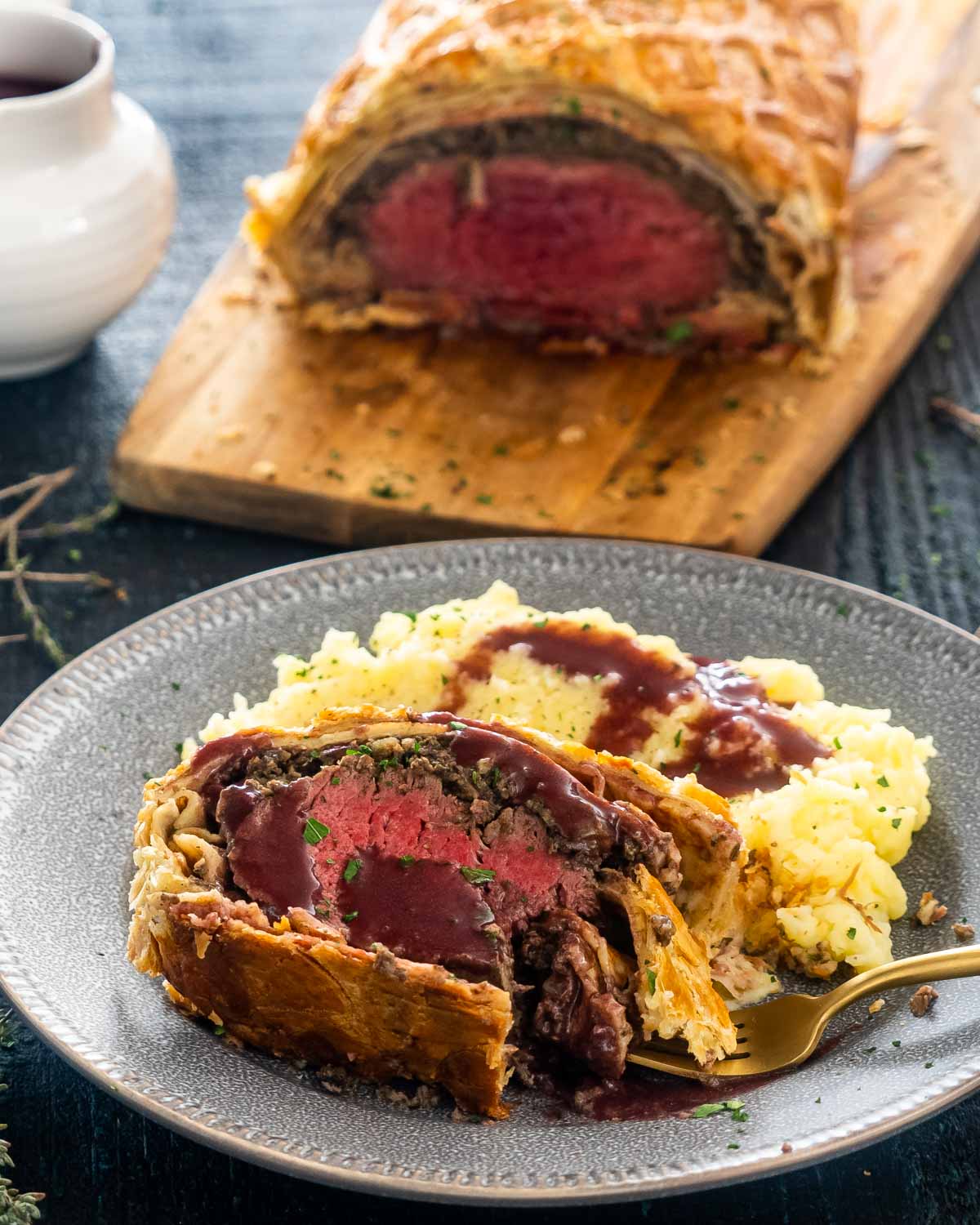 a slice of beef wellington with mashed potatoes and red wine sauce.