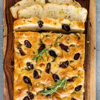 focaccia with sun dried tomatoes and olives on a cutting board with a couple slices cut out.